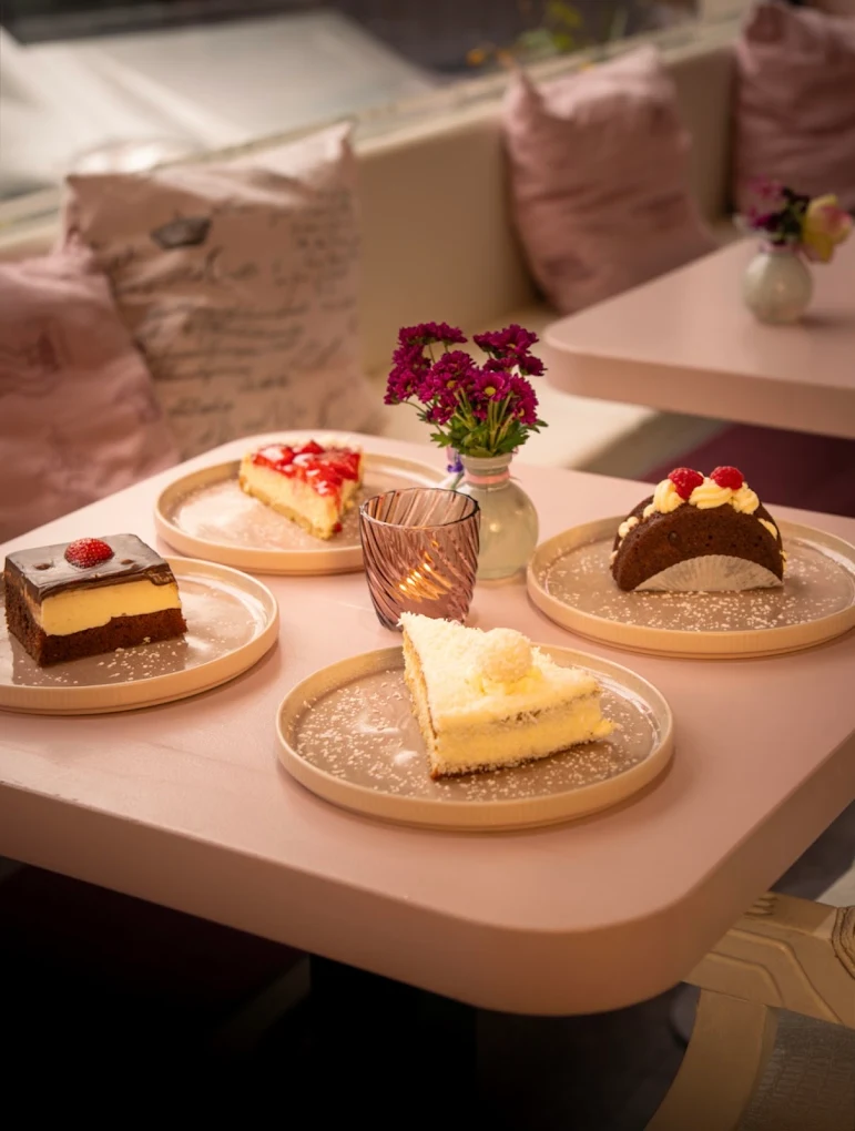 Auswahl hausgemachter Kuchenstücke auf rosa Tisch im Café Paradiso