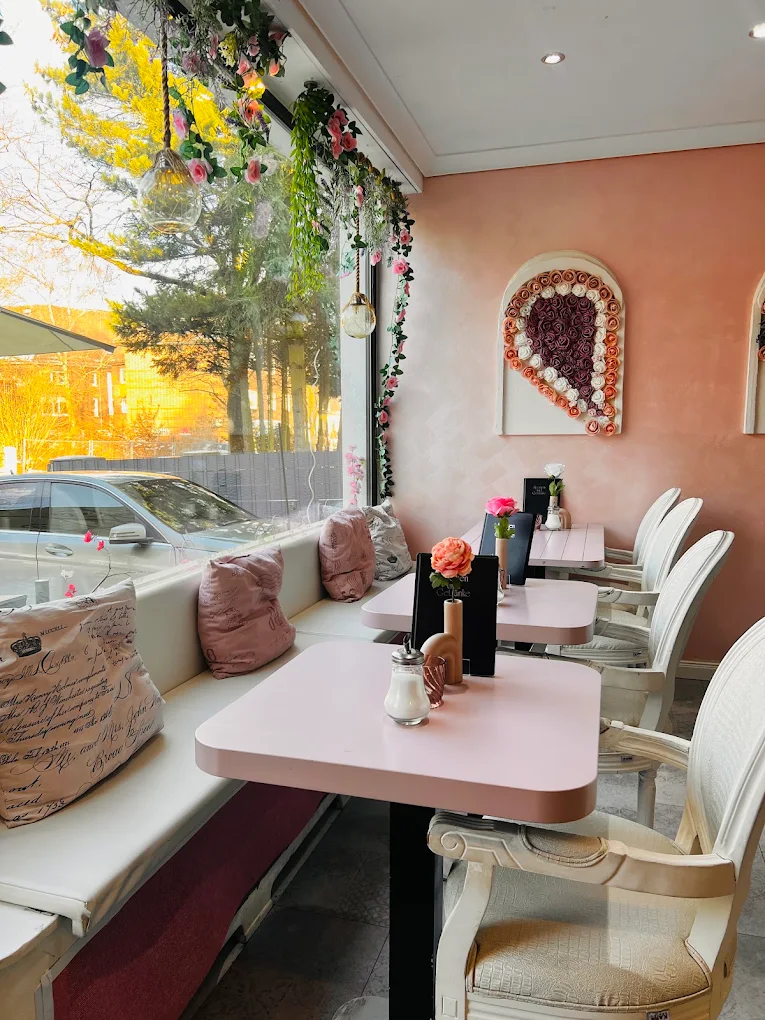 Fensterplatz im Café Paradiso mit rosa Tischen, Blumenranken und Rosenherz an der Wand